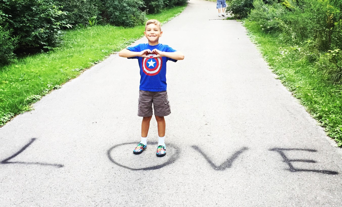 Boy standing on a paved path where the word love has been spray painted